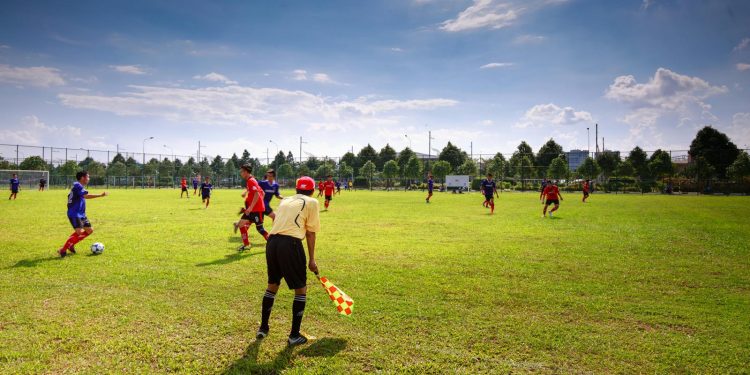 Youth soccer match in outdoor field with players, referee, and clear sky.