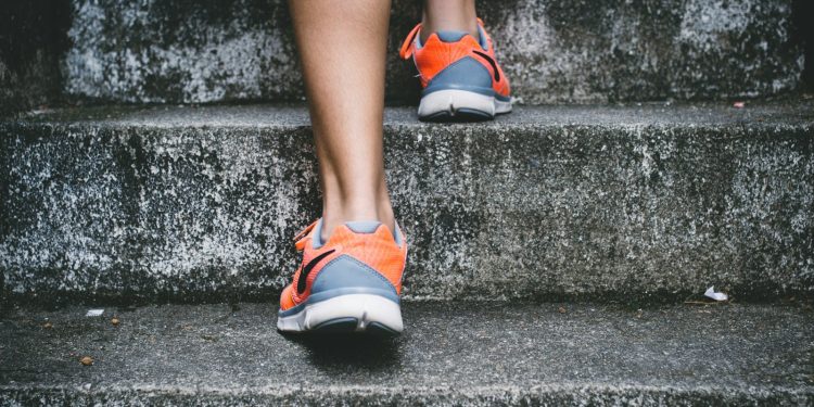 person wearing orange and gray Nike shoes walking on gray concrete stairs