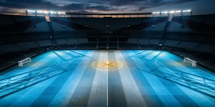Floodlit stadium pitch in Argentina blue and white with ball at centre spot, evening atmosphere.