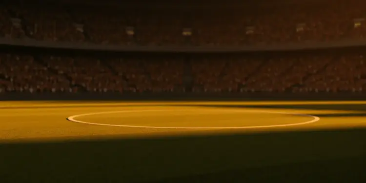 Floodlit stadium pitch at golden-hour kick-off with packed stands and dramatic shadow patterns cast across the grass.