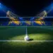 Floodlit stadium pitch with football on centre spot, blue and gold atmospheric lighting, sharp shadows, empty stands.
