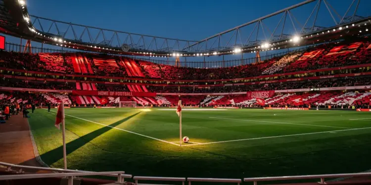 Floodlit stadium with red-draped stands, centre-spot ball, geometric shadows, dusk lighting.