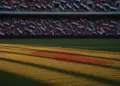 Empty floodlit stadium pitch at golden hour with dramatic shadows, packed stands in soft focus, Egyptian and Iranian flag colours visible.