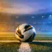 Match ball on centre spot of floodlit pitch at dusk, geometric shadows, stadium lighting, cool-blue and warm-gold atmospheric haze.