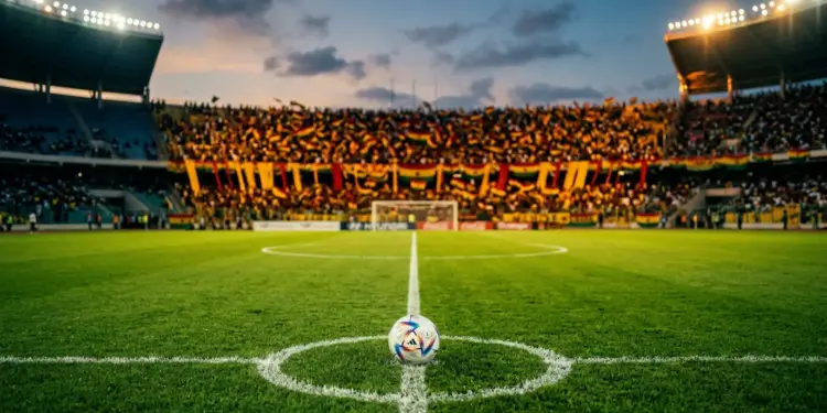 Floodlit stadium at dusk with centre pitch and gold-and-red draped stands under evening light.