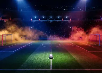 Floodlit stadium pitch with Haiti flag colours in dramatic lighting; football on centre spot; crowd silhouettes.