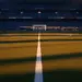 Empty floodlit football stadium with packed stands at dusk, golden-hour lighting, pristine pitch markings, dramatic shadows.