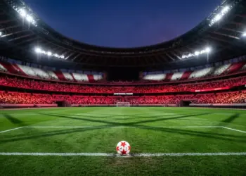 Floodlit stadium pitch at dusk with ball on centre spot, red and white colour palette, geometric shadows, calm pre-match atmosphere.