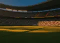 Floodlit stadium at golden hour with Mexican and Ecuadorian flag colours in crowded stands, dramatic shadows on pitch.