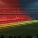 Floodlit stadium pitch at golden hour with dramatic shadows, Morocco and Haiti national colours illuminating stands, no players visible.