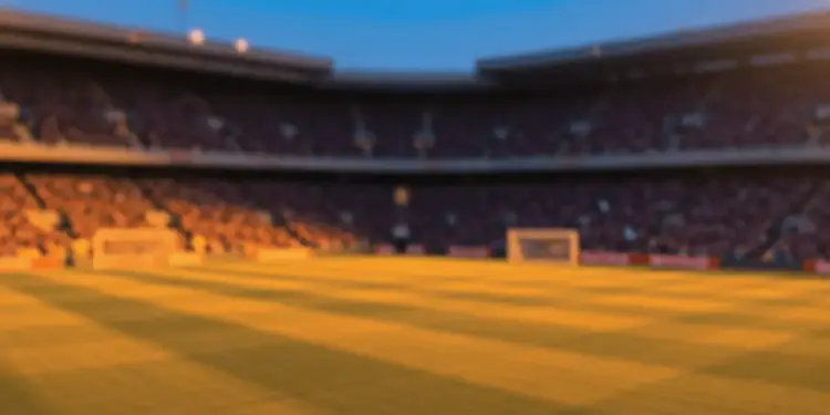 Floodlit stadium pitch at golden hour with shadows, packed stands blurred in background, warm orange and cool blue atmospheric tones.