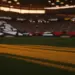 Floodlit stadium with dramatic shadows and packed stands at golden-hour kick-off, cinematic shallow depth of field.