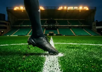 Floodlit stadium pitch at night with emerald lighting, solitary boot on centre spot, cinematic depth of field.