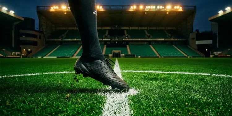 Floodlit stadium pitch at night with emerald lighting, solitary boot on centre spot, cinematic depth of field.