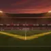 Floodlit football stadium at dusk with packed stands, geometric shadow patterns, and atmospheric golden-hour lighting during group stage fixture.