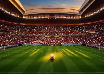 Maroon and white floodlit stadium interior with football on centre spot, evening atmosphere.