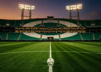 Floodlit empty stadium with emerald and white stand colours, match ball on halfway line, cinematic lighting.