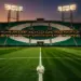 Floodlit empty stadium with emerald and white stand colours, match ball on halfway line, cinematic lighting.