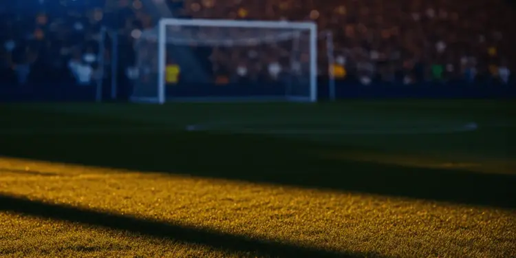 Empty floodlit football stadium at golden-hour with packed stands, dramatic shadows, and cinematic lighting.