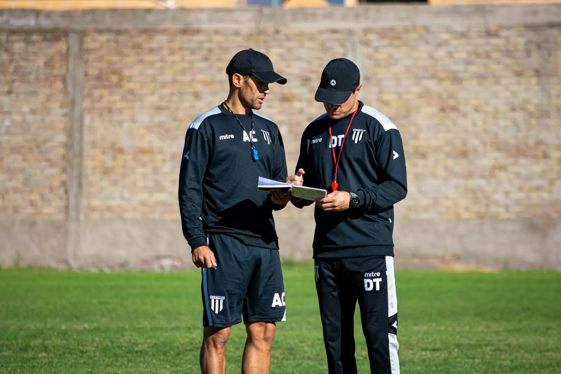 Two soccer coaches discussing tactics with a clipboard on the field.
