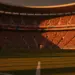 Floodlit World Cup stadium pitch at golden-hour with packed stands, dramatic shadows, South African and Korean colour palette.