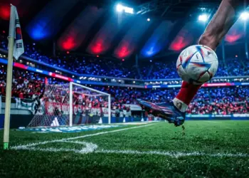 Floodlit football pitch with boot and ball in motion, blue and red colour palette, dramatic stadium lighting.