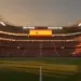 Empty floodlit stadium at dusk with packed stands and dramatic shadow patterns, ready for international match.
