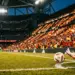 Floodlit football pitch at dusk with Spanish-coloured stand sections and ball in motion during evening match.