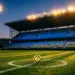 Floodlit stadium pitch at golden hour with match ball on centre spot, blue and yellow colour palette