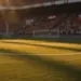 Floodlit stadium pitch with golden shadows, Swiss and Bosnian flag color palettes in distant stands