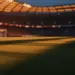 Floodlit stadium pitch at golden hour with dramatic shadows, no players visible, Turkish and US flag colour tones in lighting design.