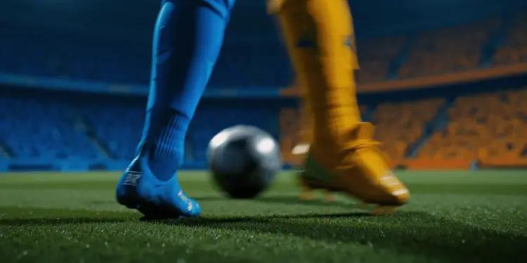 Evening floodlit pitch with two boots in motion—azure and gold—competing for a football in motion blur, shallow depth of field.