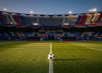 Floodlit stadium with coloured bunting and ball on pitch, pre-match atmosphere