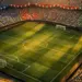 Aerial stadium view at dusk with flag-coloured bunting across stands and floodlit pitch markings below.