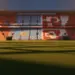 Empty floodlit football stadium at dusk with Argentina blue-white and Switzerland red-white coloured stands under dramatic lighting.