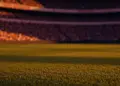 Floodlit stadium at dusk with packed stands and dramatic shadows during international football match.