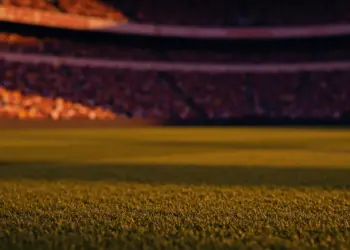 Floodlit stadium at dusk with packed stands and dramatic shadows during international football match.