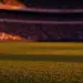 Floodlit stadium at dusk with packed stands and dramatic shadows during international football match.
