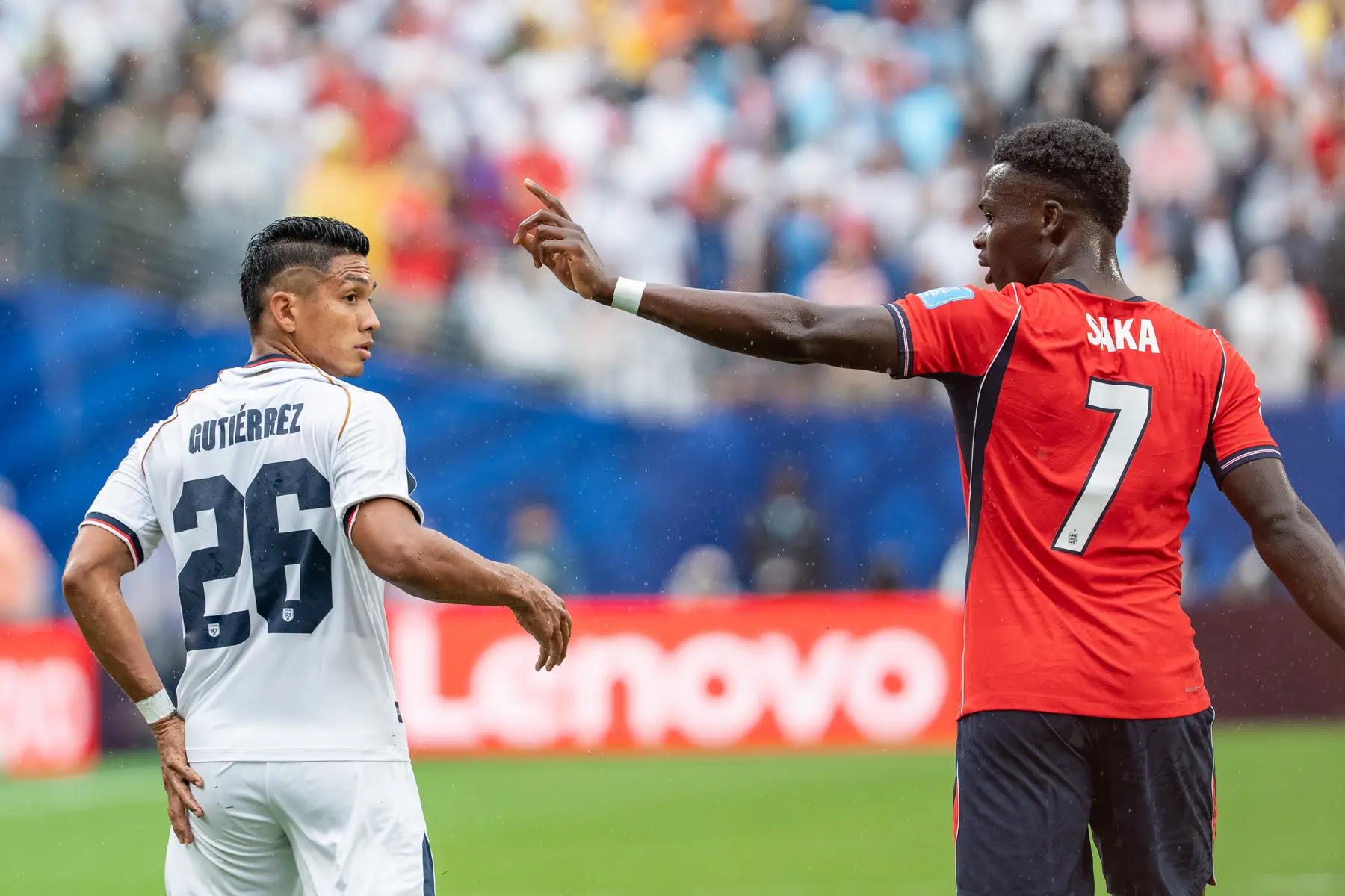 Bukayo Saka in an England kit pointing while speaking to Jorge Gutierrez during a match.