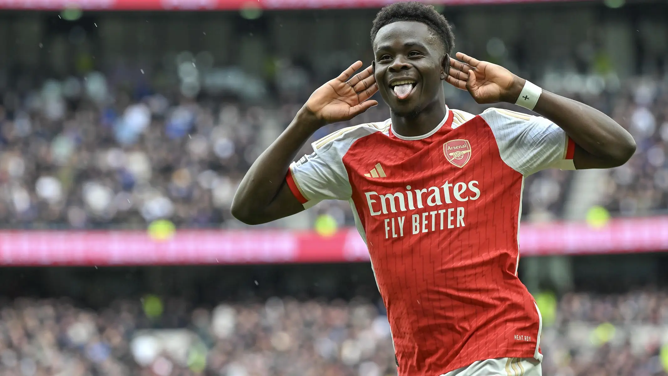 Bukayo Saka celebrating in an Arsenal home kit with his hands behind his ears.